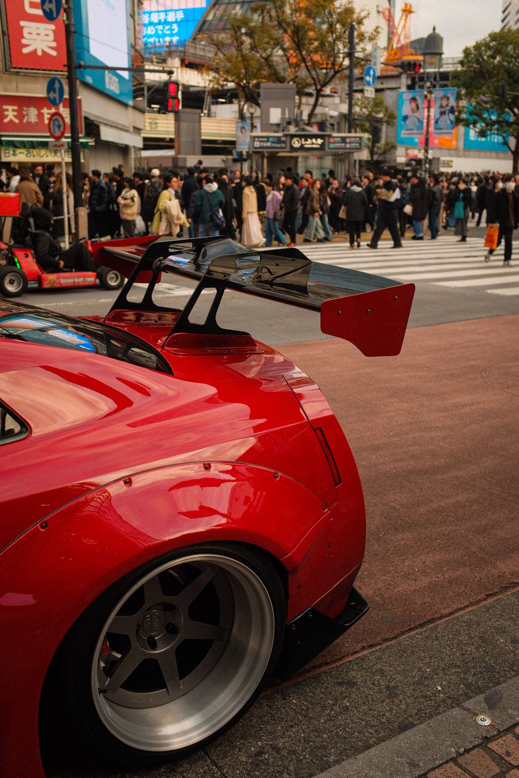 A red car's rear wing at Shibuya Crossing